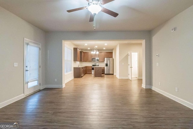 unfurnished living room featuring ceiling fan with notable chandelier and dark hardwood / wood-style flooring