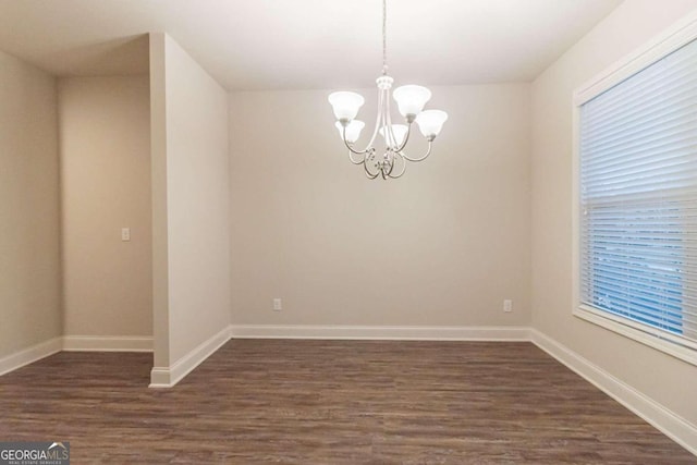 empty room with dark hardwood / wood-style flooring and an inviting chandelier