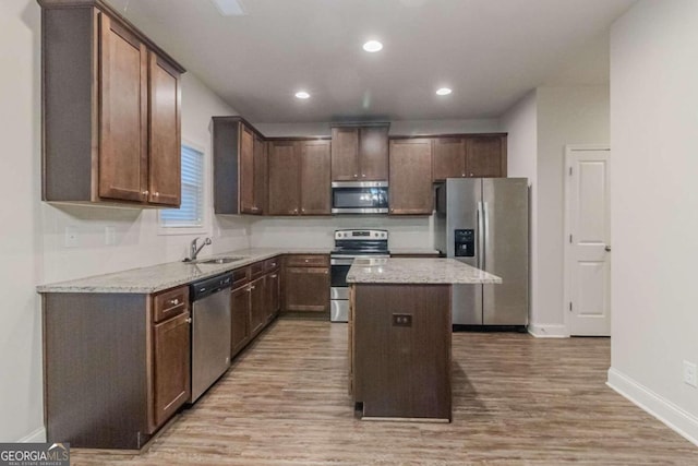 kitchen featuring a center island, sink, stainless steel appliances, light stone counters, and light hardwood / wood-style floors