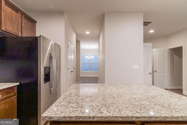 kitchen with light stone countertops, stainless steel refrigerator with ice dispenser, a notable chandelier, hardwood / wood-style floors, and a center island