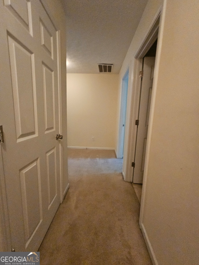 hallway with light carpet and a textured ceiling