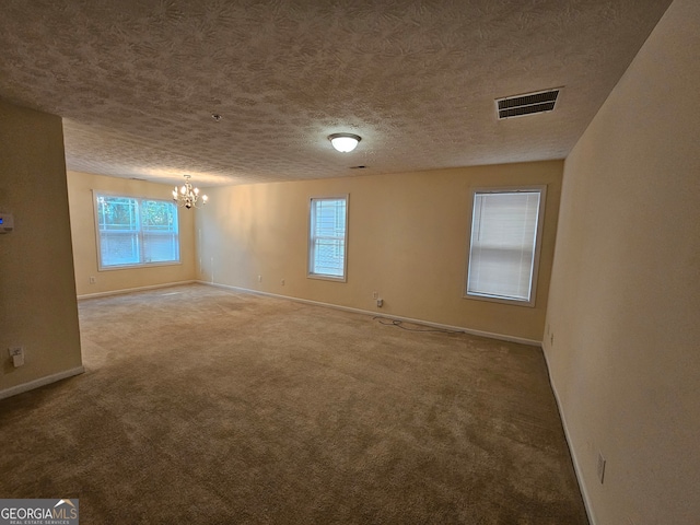 carpeted empty room featuring a healthy amount of sunlight, a textured ceiling, and a chandelier