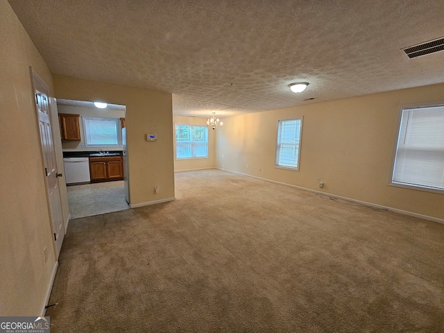 carpeted spare room featuring sink, a textured ceiling, and an inviting chandelier