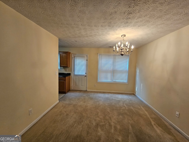 unfurnished dining area with a chandelier, a textured ceiling, and carpet flooring