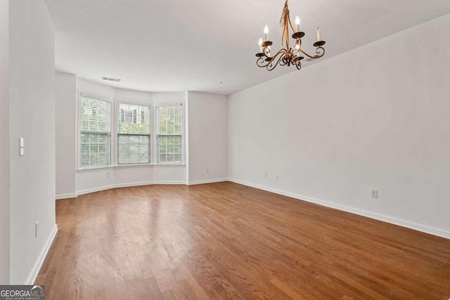 empty room featuring an inviting chandelier and hardwood / wood-style flooring