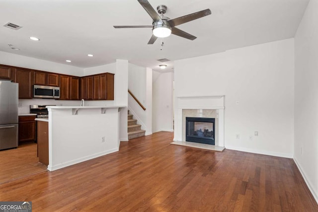 kitchen featuring appliances with stainless steel finishes, dark hardwood / wood-style flooring, a breakfast bar, ceiling fan, and a premium fireplace