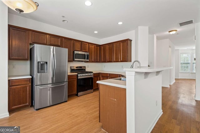 kitchen with sink, a kitchen breakfast bar, kitchen peninsula, appliances with stainless steel finishes, and light wood-type flooring