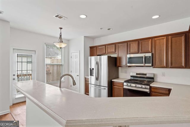 kitchen with hanging light fixtures, stainless steel appliances, and light hardwood / wood-style flooring