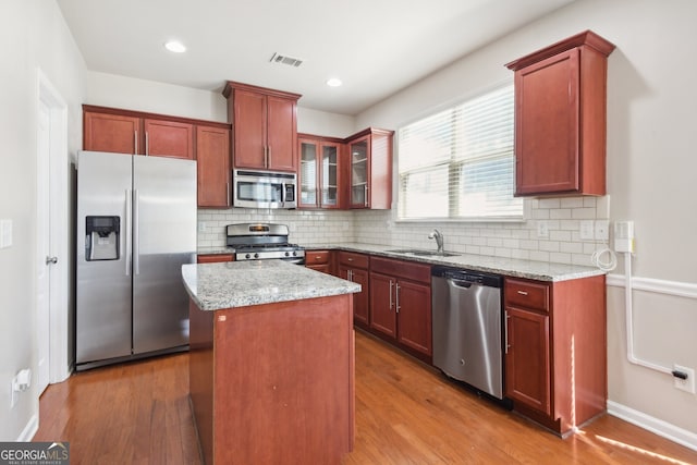 kitchen featuring hardwood / wood-style floors, a center island, light stone counters, and stainless steel appliances