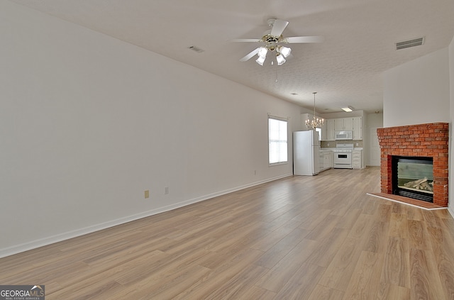 unfurnished living room featuring ceiling fan with notable chandelier, light wood-type flooring, a textured ceiling, and a brick fireplace