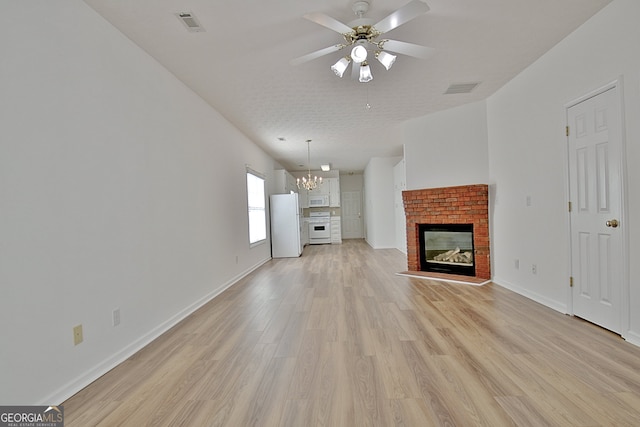 unfurnished living room with a textured ceiling, ceiling fan with notable chandelier, a fireplace, and light hardwood / wood-style flooring