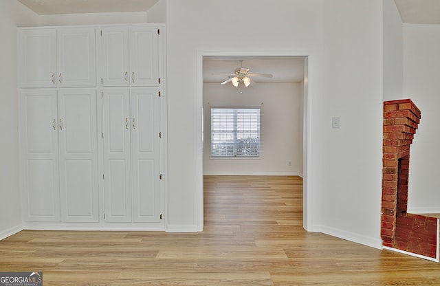 interior space with a closet, light hardwood / wood-style floors, a brick fireplace, and ceiling fan