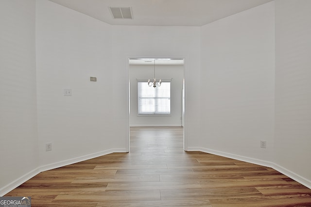 empty room with a notable chandelier and light hardwood / wood-style floors