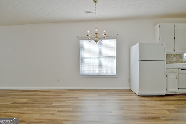 unfurnished dining area featuring a chandelier, a textured ceiling, and light hardwood / wood-style flooring