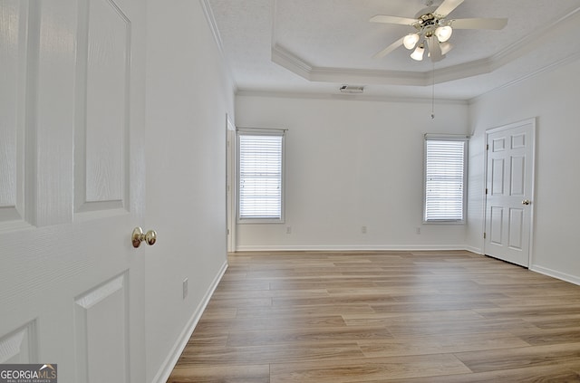 unfurnished bedroom with light wood-type flooring, a tray ceiling, ceiling fan, and crown molding