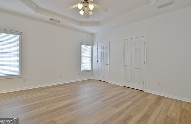 unfurnished bedroom featuring light wood-type flooring, a raised ceiling, and ornamental molding