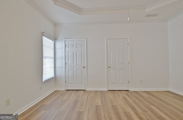 unfurnished bedroom featuring a raised ceiling, light wood-type flooring, and ornamental molding