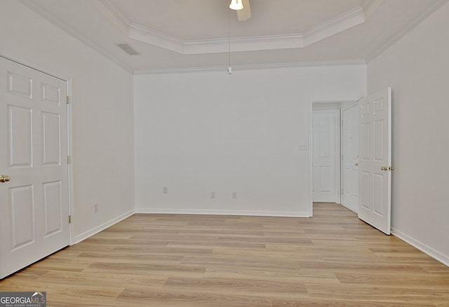 spare room with a raised ceiling, light wood-type flooring, and ornamental molding