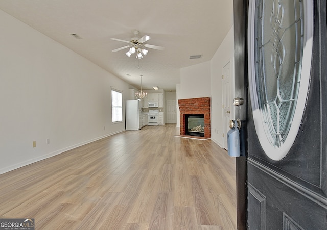 unfurnished living room featuring a brick fireplace, ceiling fan with notable chandelier, and light wood-type flooring