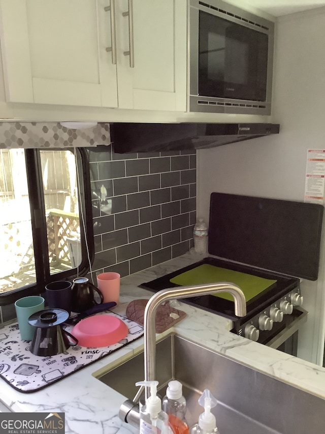 interior details with light stone counters, stainless steel microwave, white cabinetry, and backsplash