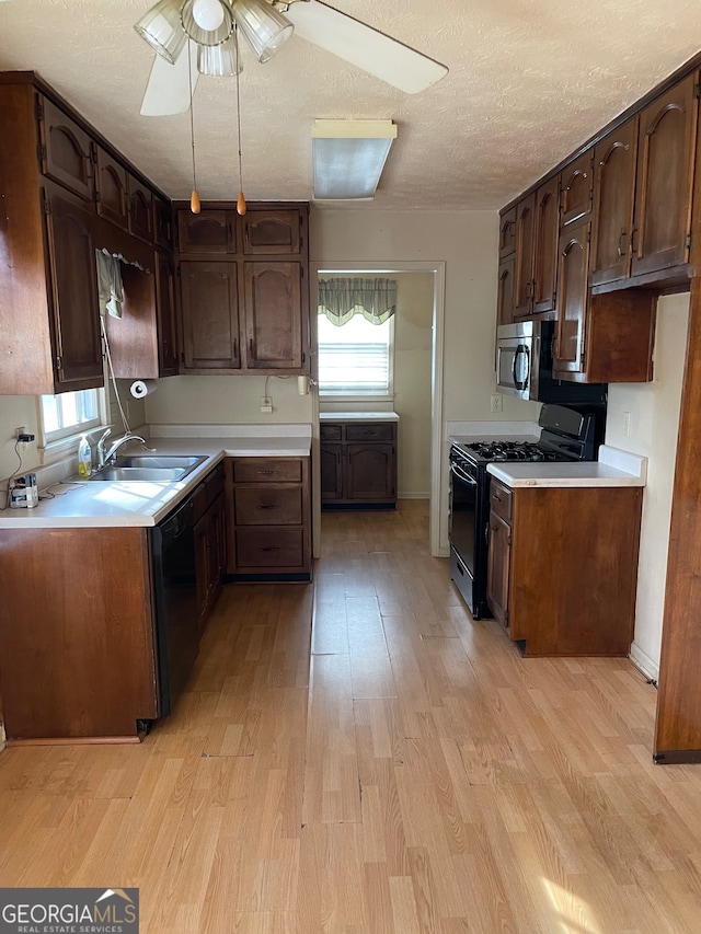 kitchen with sink, black appliances, a textured ceiling, and light hardwood / wood-style floors