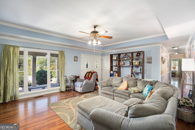 living room featuring ceiling fan, wood-type flooring, ornamental molding, and a tray ceiling