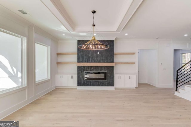 unfurnished living room with a chandelier, a large fireplace, a raised ceiling, and light hardwood / wood-style flooring