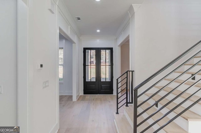 entryway with light hardwood / wood-style floors, ornamental molding, and french doors