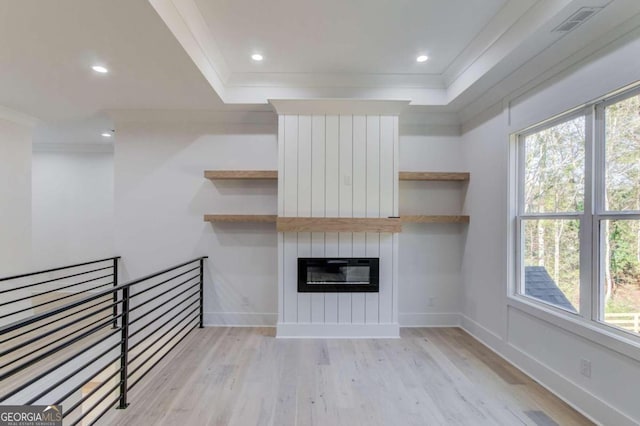 unfurnished living room with a tray ceiling, a fireplace, light hardwood / wood-style floors, and ornamental molding