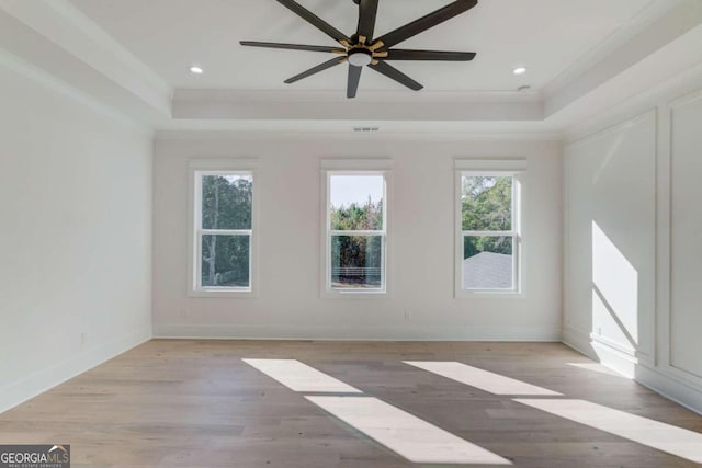 unfurnished room with ceiling fan, light hardwood / wood-style floors, a raised ceiling, and crown molding