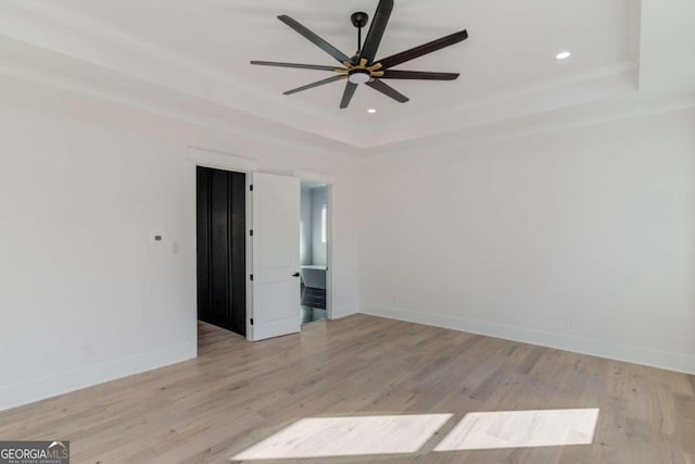 spare room featuring a tray ceiling, ceiling fan, and light hardwood / wood-style flooring