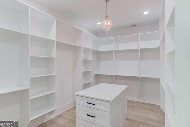 spacious closet with light hardwood / wood-style floors and an inviting chandelier