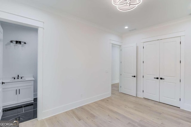 unfurnished bedroom with a closet, sink, ornamental molding, and light wood-type flooring