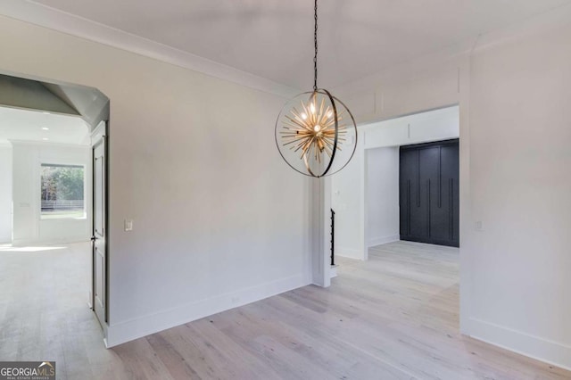 unfurnished dining area featuring light hardwood / wood-style floors, crown molding, and a chandelier