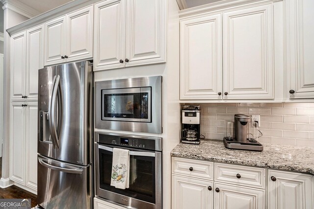 kitchen featuring white cabinets, stainless steel appliances, light stone countertops, and crown molding