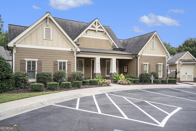 view of front of property featuring roof with shingles, uncovered parking, covered porch, board and batten siding, and stone siding