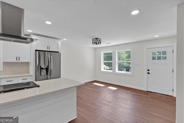 kitchen with light stone countertops, stainless steel refrigerator with ice dispenser, ventilation hood, wood-type flooring, and white cabinetry