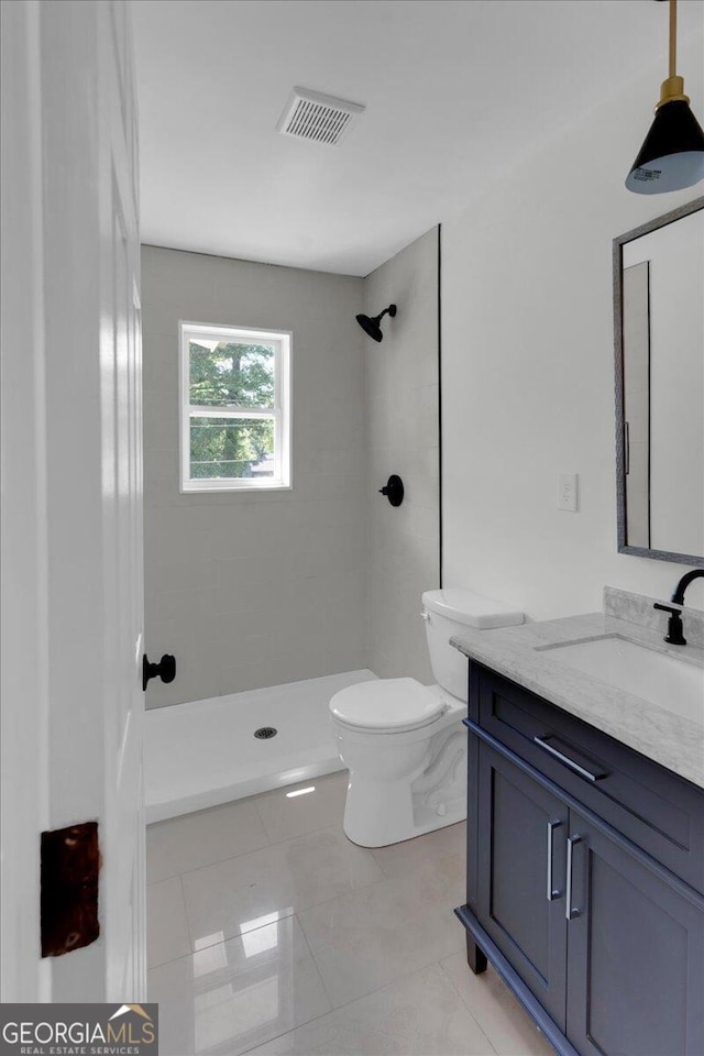 bathroom featuring tile patterned flooring, vanity, tiled shower, and toilet