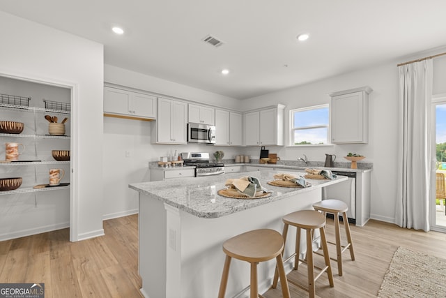 kitchen with a center island, white cabinets, light stone countertops, light wood-type flooring, and appliances with stainless steel finishes