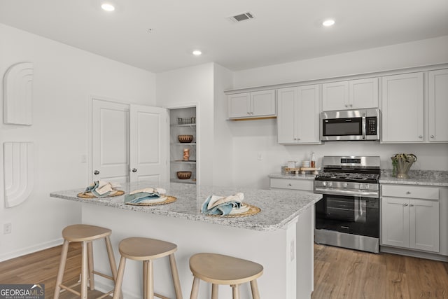 kitchen featuring appliances with stainless steel finishes, light hardwood / wood-style flooring, light stone counters, and a kitchen island with sink