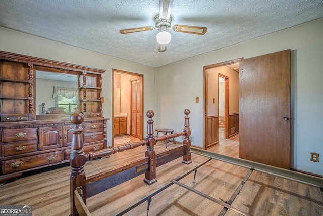 bedroom with wood walls, ensuite bath, ceiling fan, a textured ceiling, and light hardwood / wood-style floors