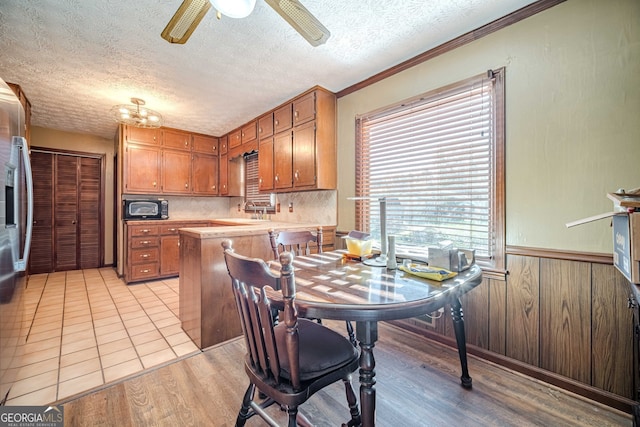 kitchen featuring a textured ceiling, light hardwood / wood-style flooring, ornamental molding, and wood walls