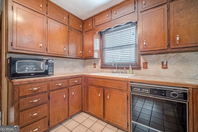 kitchen featuring light tile patterned flooring, a textured ceiling, tile countertops, and sink