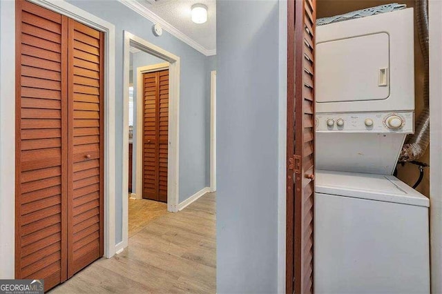 laundry room with stacked washing maching and dryer, ornamental molding, and light hardwood / wood-style flooring