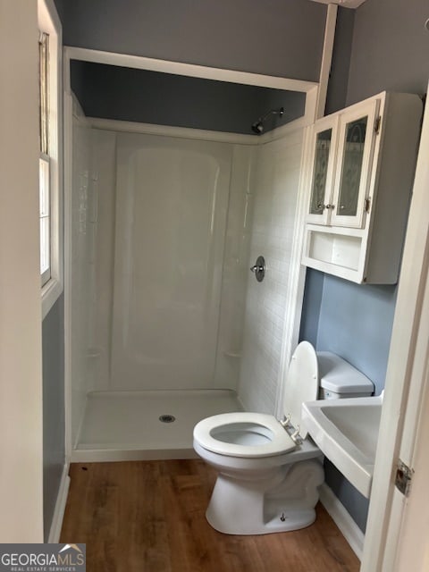 bathroom with toilet, wood-type flooring, and tiled shower