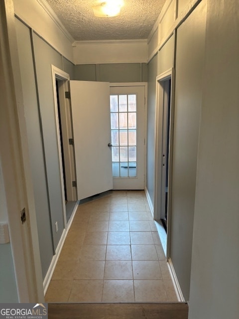 corridor with a textured ceiling, ornamental molding, and light tile patterned flooring