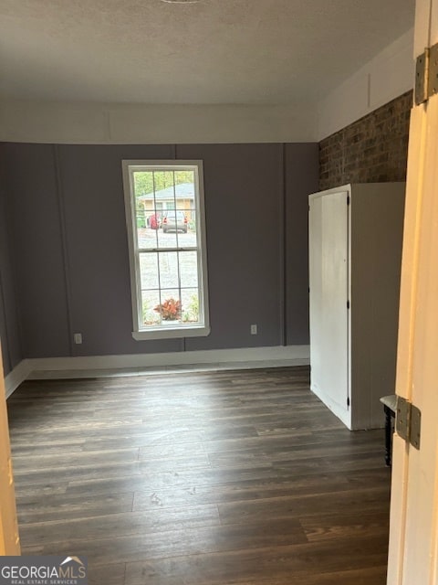 spare room with dark wood-type flooring and brick wall