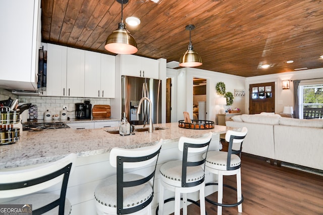 kitchen with pendant lighting, backsplash, white cabinets, stainless steel fridge, and light stone countertops