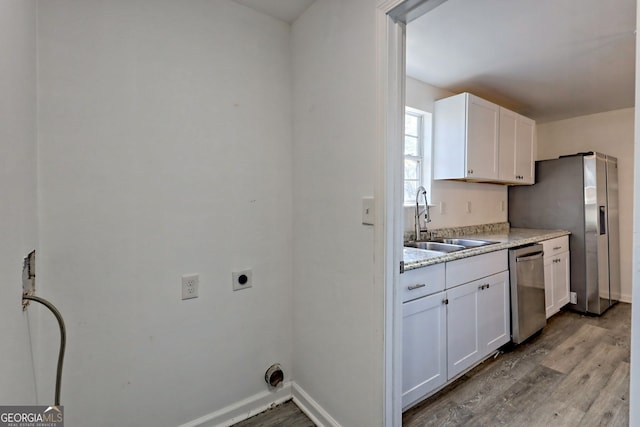 kitchen with white cabinetry, sink, light stone counters, light hardwood / wood-style flooring, and appliances with stainless steel finishes