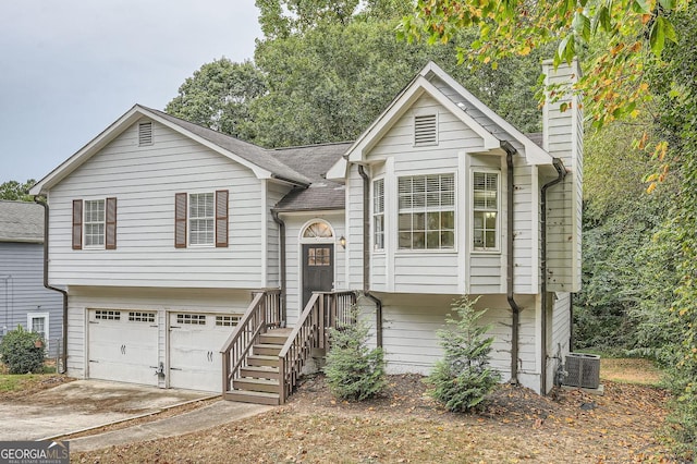 bi-level home with a chimney, driveway, cooling unit, a garage, and a shingled roof